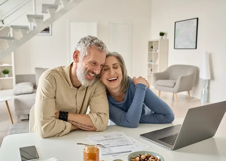 a man and woman laugh together while watching something on a laptop